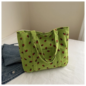 Close-up of green corduroy tote bag featuring red strawberry print and soft texture