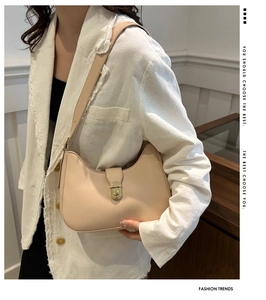 Model wearing a chic beige crescent shoulder bag with golden metallic twist lock buckle