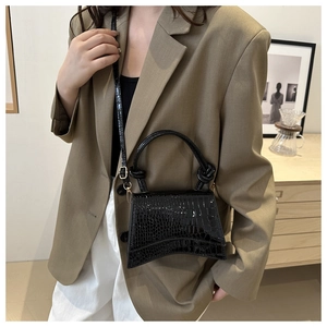 Detail of black crocodile embossed handbag with unique curved base and golden metal hardware