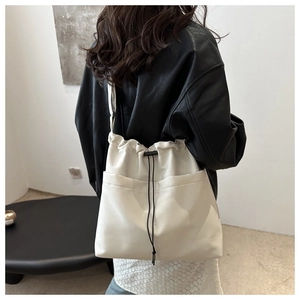 Detail view of white drawstring bucket bag with front pockets and black strap for daily use