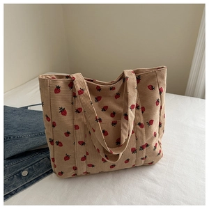 Detail of corduroy tote bag with red strawberry print on soft beige fabric texture