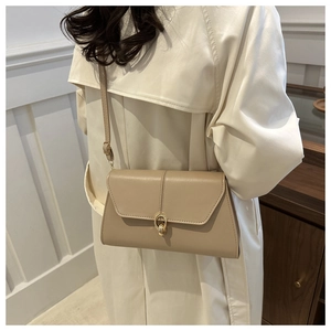 Beige faux leather crossbody bag with gold buckle detail worn by a model in a warm setting