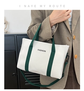 Detail of canvas bag showing green handles, fashion text and metallic strap hooks