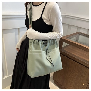Detail of light green drawstring bucket bag with front pockets and adjustable strap