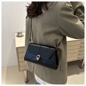 Detail of a black PU leather shoulder bag with a gold horseshoe buckle on a green blazer