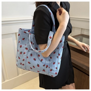 Close-up of light blue corduroy tote bag featuring red strawberry print and side pocket