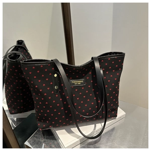 Détail de motifs cœurs rouges sur sac cabas en toile noire avec logo en cuir et rivets