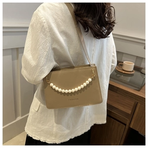 Detail of khaki PU leather bag with pearl chain and FASHION logo on a female model