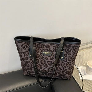Chic leopard print tote bag with black leather straps and brand label on a dark sofa