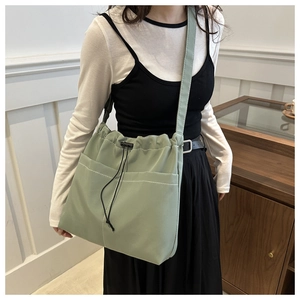Detail of sage green drawstring bag with white stitching and external pockets