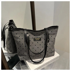 Gros plan du sac cabas gris à pois avec un écusson en cuir sur un livre blanc