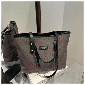 Detail of grey tote bag with red heart print, gold rivets, and black leather brand tag