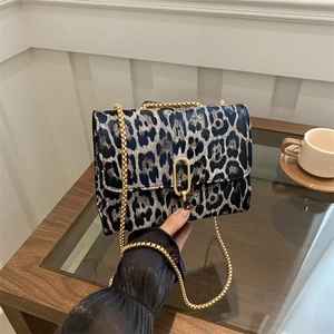 Chic leopard print crossbody bag with gold chain strap and plush texture on glass table