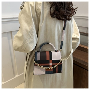 Détail du sac bandoulière à carreaux avec chaîne dorée sur un trench-coat beige élégant