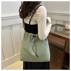 Detailed shot of a light green canvas drawstring tote bag with a front pocket on model