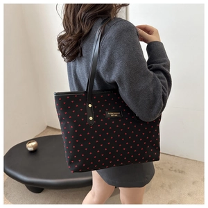 Détail du sac cabas noir à motifs cœurs rouges porté à l'épaule par un mannequin