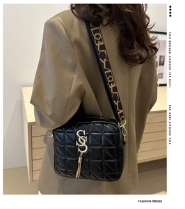 Détail du sac bandoulière matelassé noir avec boucle à pompon doré et large sangle jacquard