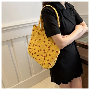 Detailed view of yellow corduroy tote bag with strawberry print worn by a model