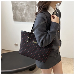 Detailed close-up of black tote bag featuring red heart patterns and leather straps