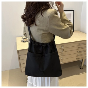 Detail of a large black drawstring tote bag with dual front pockets worn on the shoulder