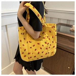 Detail of yellow corduroy tote bag featuring red strawberry prints and functional front pocket