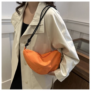 Detail of bright orange crescent crossbody bag with black rope strap on neutral outfit