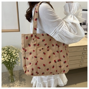Detailed shot of beige corduroy tote bag with red strawberry print on open front pocket