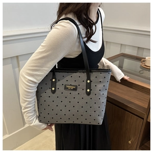 Close-up of gray canvas tote bag featuring black polka dots and leather logo tag