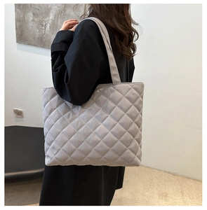 Close-up of a grey quilted tote bag featuring a diamond stitch pattern on a model
