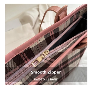 Close-up of pink leather trim and golden metal zipper on plaid tote bag detail