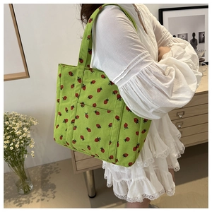 Close-up of strawberry embroidery on green corduroy tote bag with wide shoulder strap