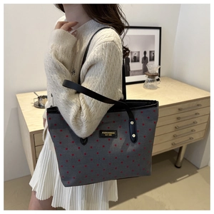 Detailed view of gray canvas tote bag with red polka dots and black leather shoulder strap