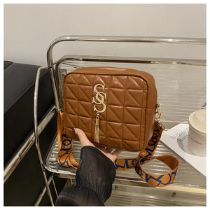 Détail du sac à bandoulière matelassé marron avec logo doré et large sangle tissée