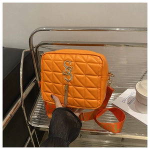 Détail d'un sac à bandoulière matelassé orange avec logo métallique et pendentif à franges