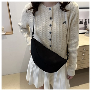 Detail of black oxford nylon crescent crossbody bag styled with a beige knit cardigan