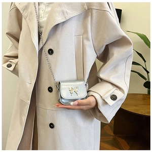 Close-up of metallic silver mini crossbody bag with butterfly clasp on beige coat