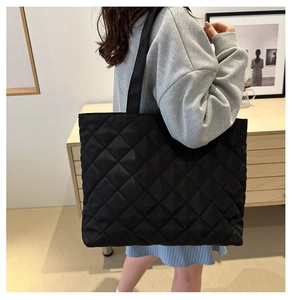 Black quilted tote bag with large capacity shown being worn in a minimalist interior