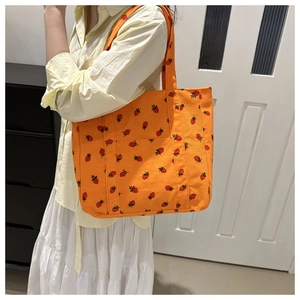 Detail of orange corduroy tote bag with strawberry print worn by a model in a cozy room