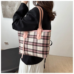Detailed view of the large plaid tote bag worn on a shoulder over a black and white outfit