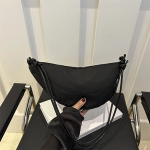 Black nylon crescent bag with drawstring knot straps on a white chair setting