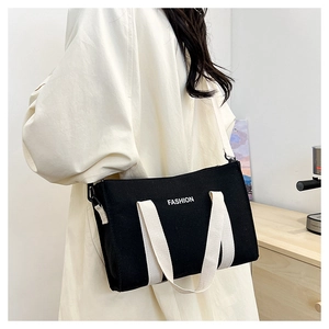 Detail of black canvas tote bag with FASHION text and adjustable shoulder strap worn by model