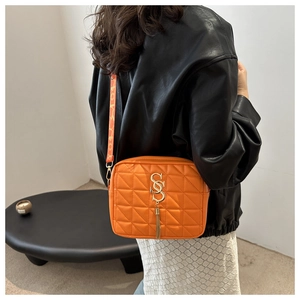 Détail d'un sac bandoulière orange matelassé avec pompon doré et logo sur un mannequin