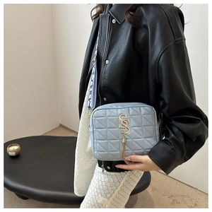 Détail du sac bandoulière bleu clair matelassé avec pompon doré et large sangle