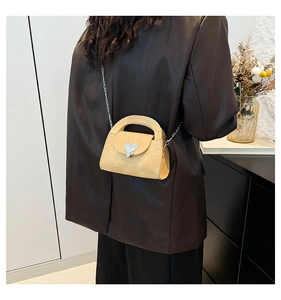 Detail of a chic beige suede bag with silver heart clasp and chain strap on a model