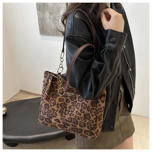 Leopard print tote bag with gold chain strap and brown leather handle worn by a model