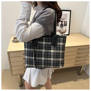 Detailed view of the large plaid tote bag with black leather shoulder straps on a model