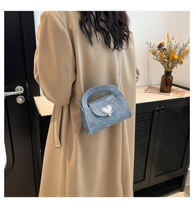 Detail of light blue denim crossbody bag with silver heart buckle on a beige trench coat