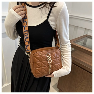 Détail du sac à bandoulière marron matelassé avec pompon doré et sangle à logo orange
