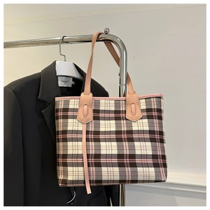 Detail of checkered plaid tote bag with pink leather handles hung against black blazer