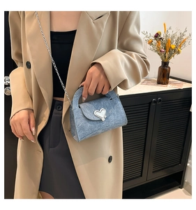 Detail of light blue denim handbag featuring a silver heart clasp and chain strap